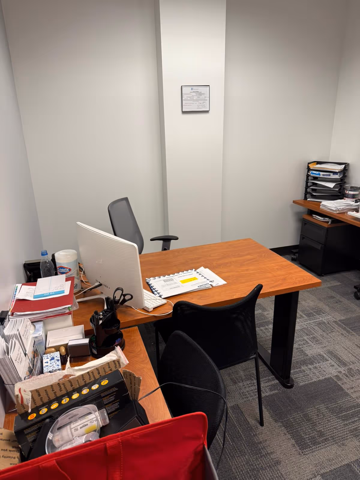 Office desk with computer, paperwork, and filing trays in a compact workspace.