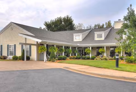 Single-story senior living facility with covered entrance, manicured shrubs, and a paved driveway.