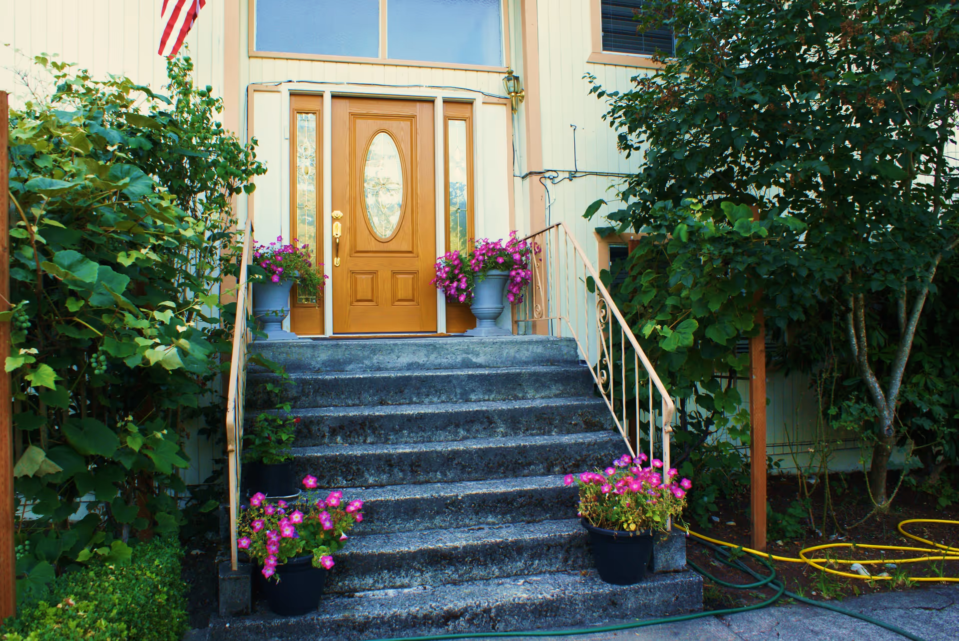 Front entrance of a residence with stone steps, wooden door, and flowering planters.