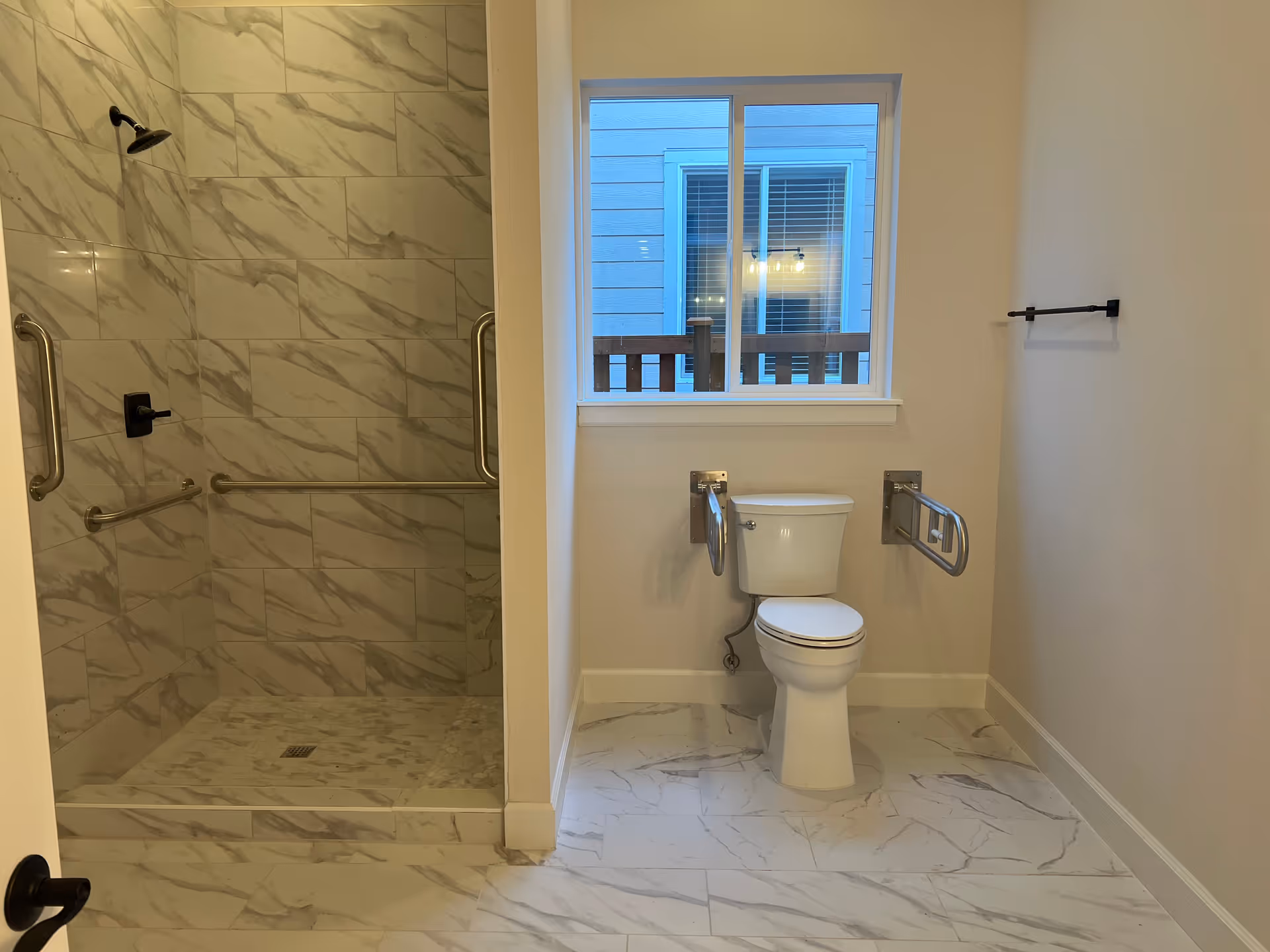 Modern bathroom with walk-in shower, toilet, marble tiles, and a window.