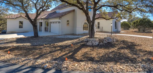 White stucco assisted living facility with tiled roof, trees, and a gravel front yard.