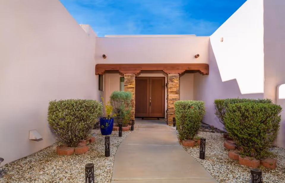 Entrance to a senior living facility with light pink walls, stone pillars, and potted shrubs.