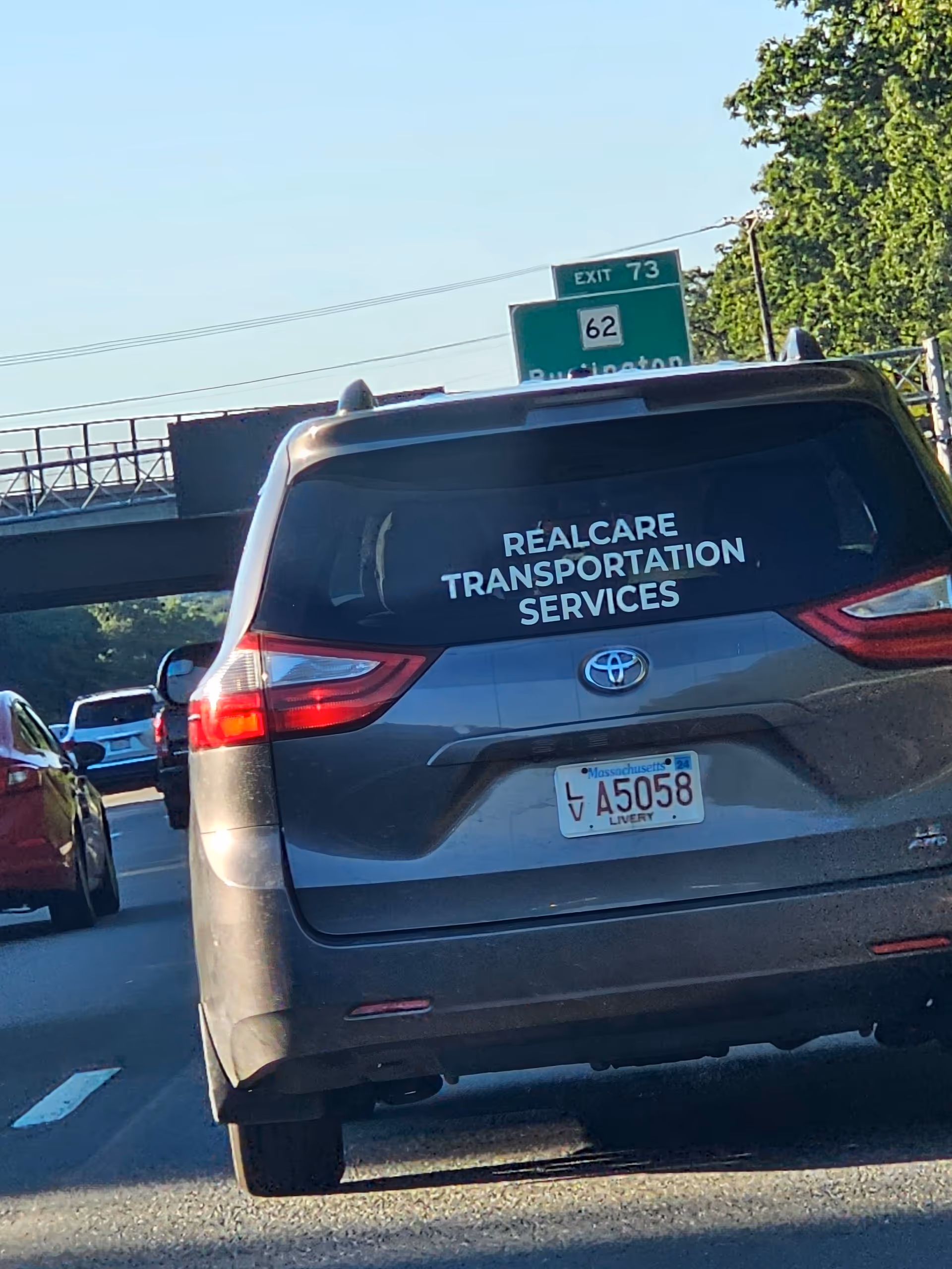 Rear view of a gray van with RealCare Transportation Services on the back, on a highway.