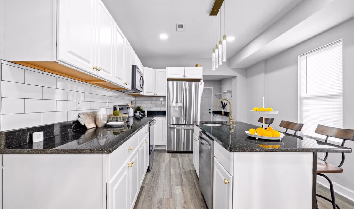 Bright modern kitchen with white cabinets, dark countertops, and an island with fruit.