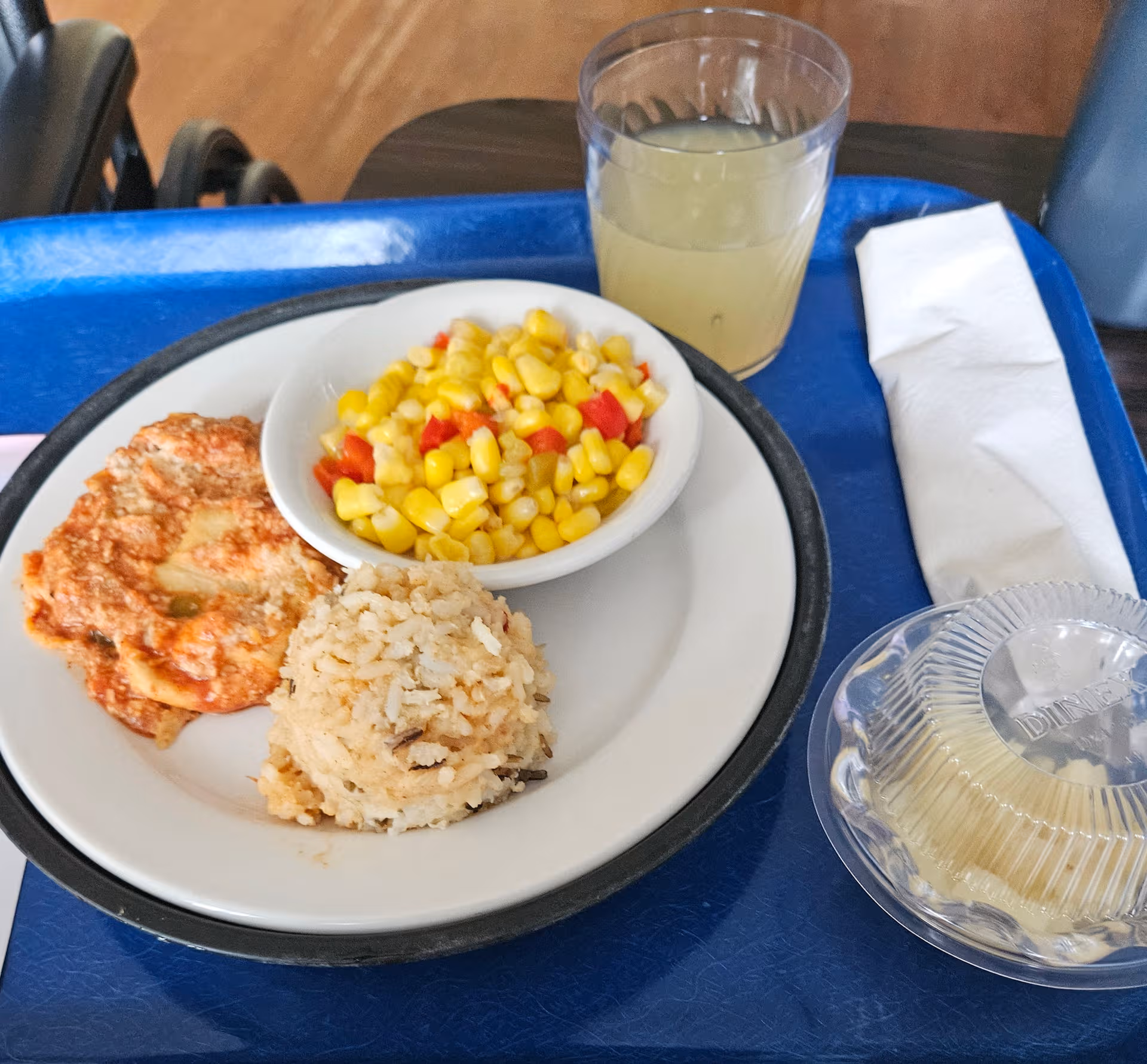 Tray with corn, rice, and a slice of pizza on a blue cafeteria table.