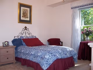 Bedroom with a metal headboard bed, blue quilt, nightstand, window, and vase of flowers.
