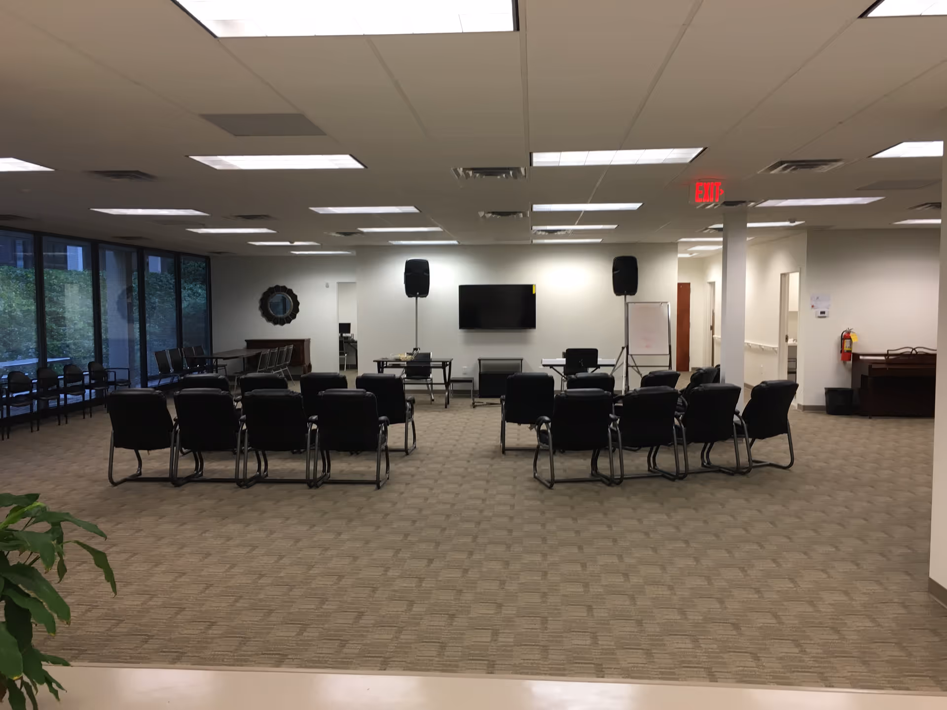 A spacious interior room with rows of black chairs, a TV, speakers, and a whiteboard.