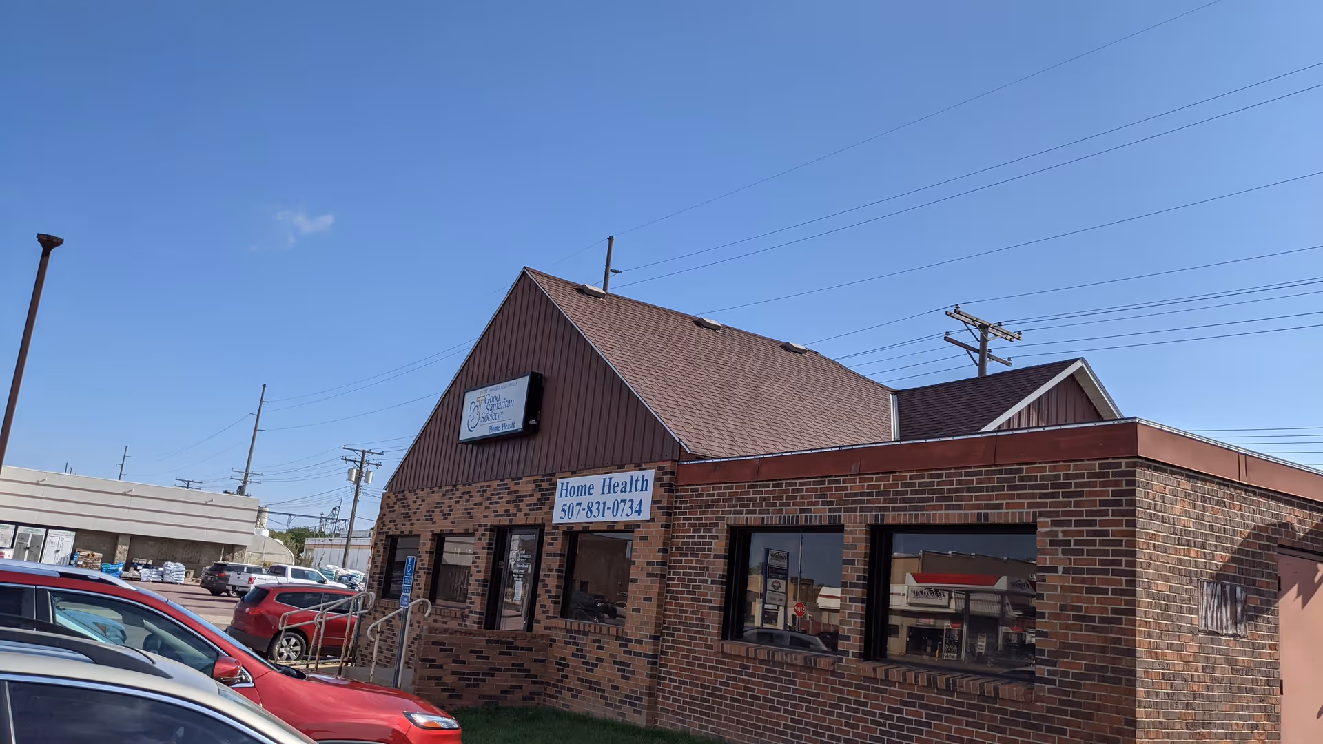Exterior brick building of Good Samaritan Society Home Health with parked cars nearby.