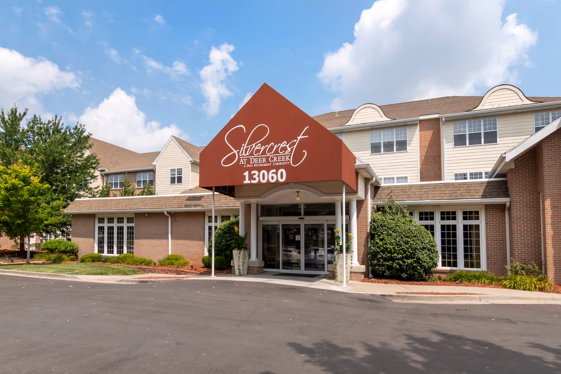 Front entrance of the Silvercrest at Deer Creek senior living building with a red canopy showing the name and address.