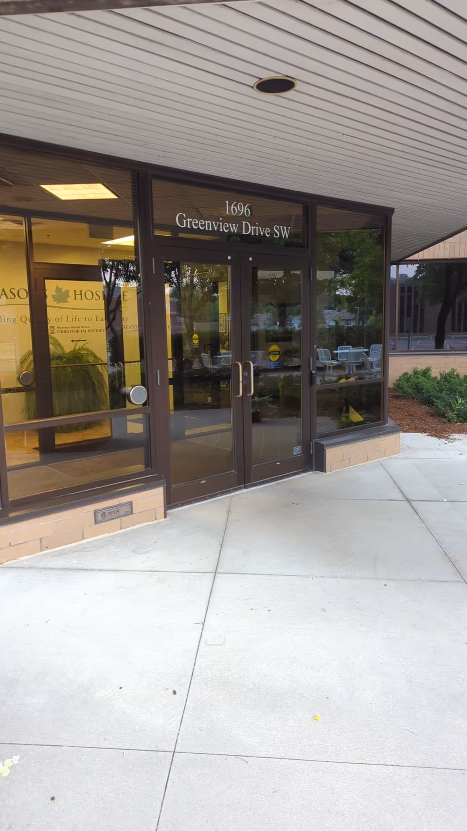 Front entrance of Seasons Hospice with glass doors and address 1696 Greenview Drive SW.