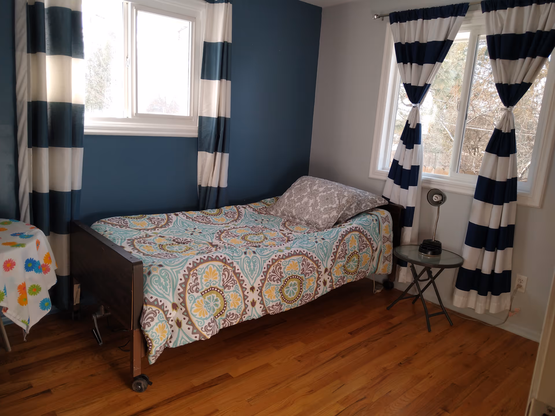 Single bedroom with a colorful patterned quilt, blue accent wall, and striped curtains.