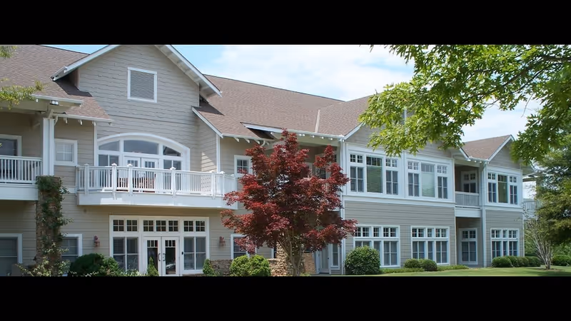 Front exterior of a two-story senior living building with balconies, many windows, and landscaped lawn and trees.
