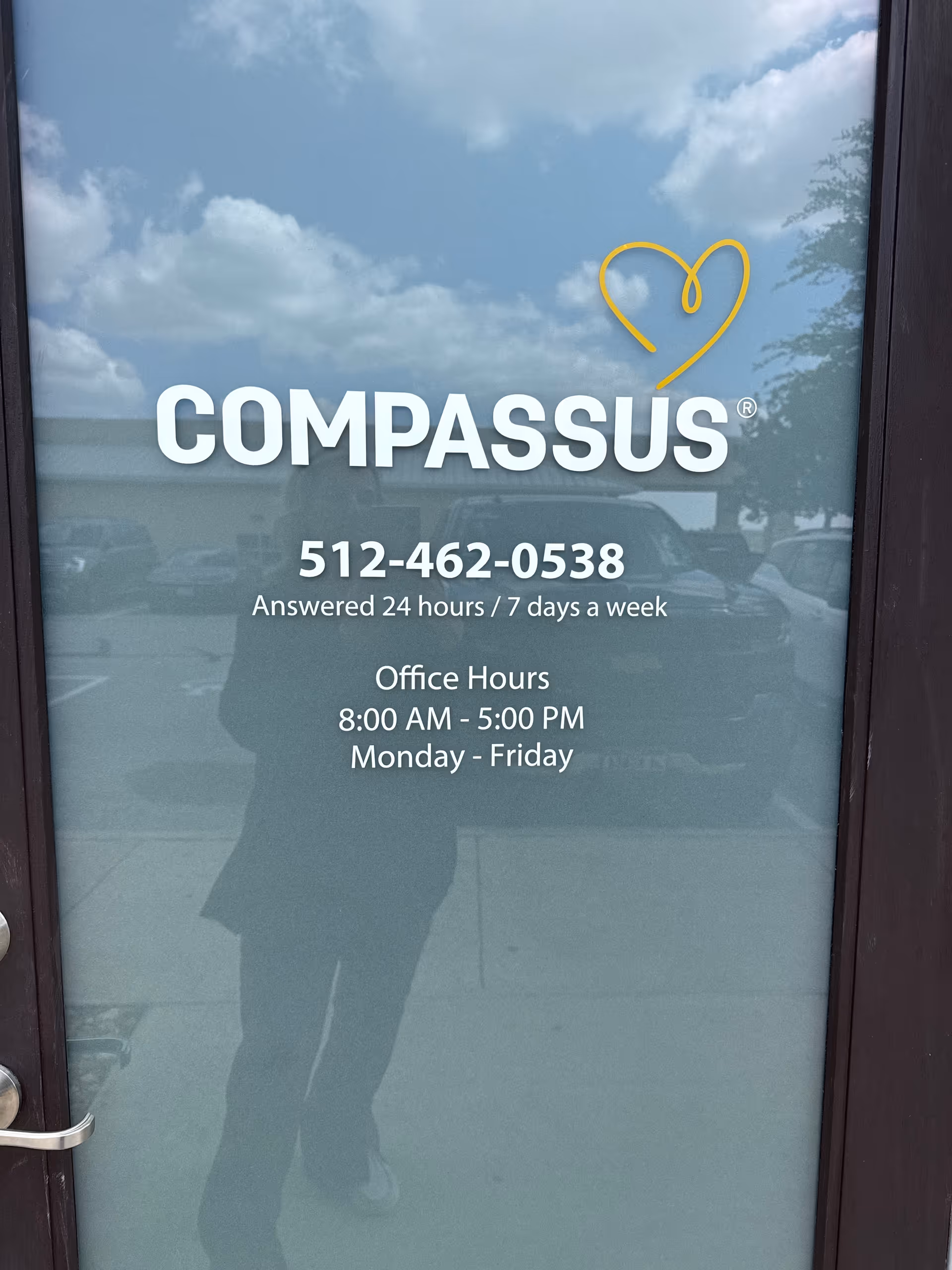 Glass door with Compassus logo and phone number reflecting a person outside.