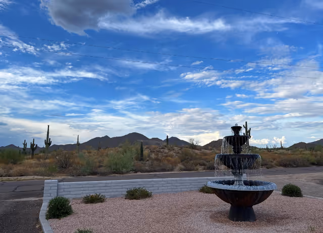 Desert landscape with cacti, a tiered fountain, and a blue sky.
