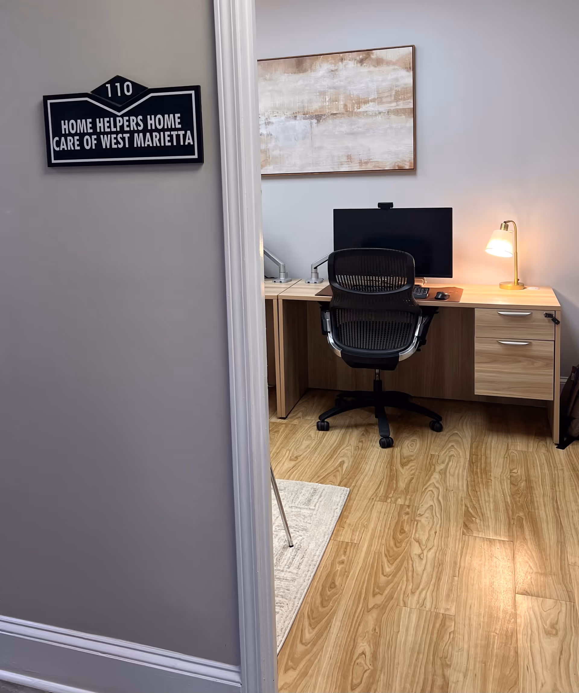 Office desk setup inside the facility featuring computer monitor, chair, lamp, and wall sign.