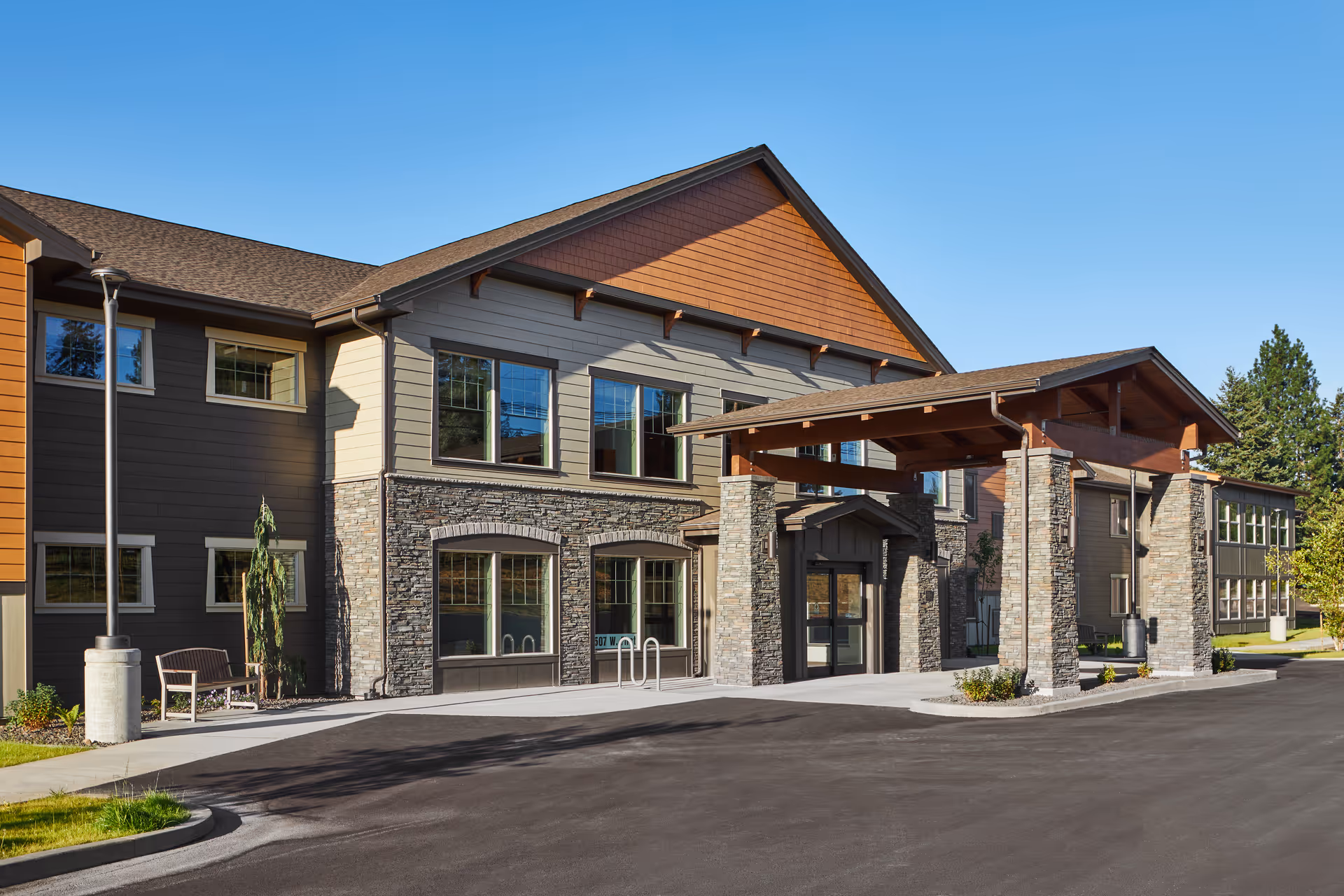 Modern assisted living facility exterior with stone accents, large windows, and a covered entrance.