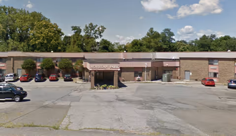 Front view of the Mohegan Park building with an entrance canopy, parking lot, and several parked cars.