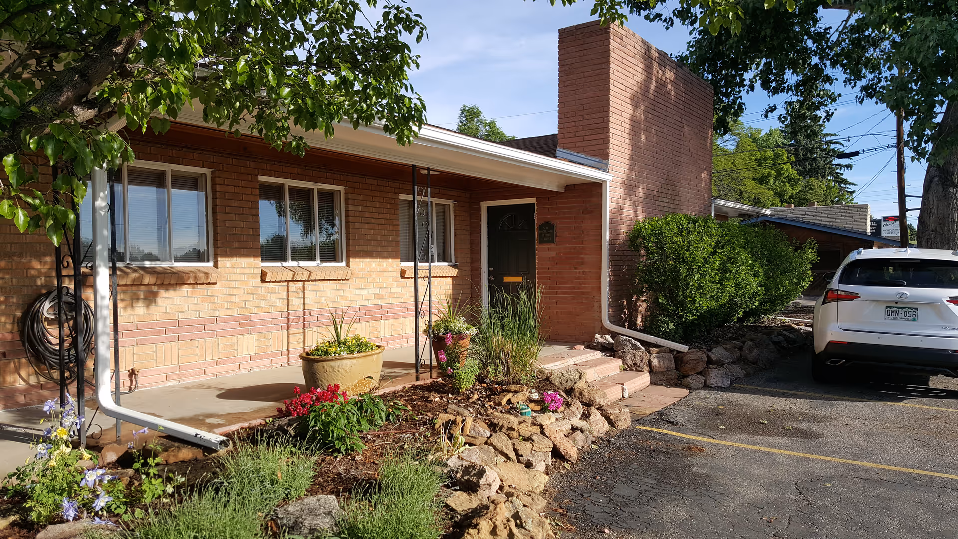 Single-story brick building entrance with flower pots and a white car parked nearby.