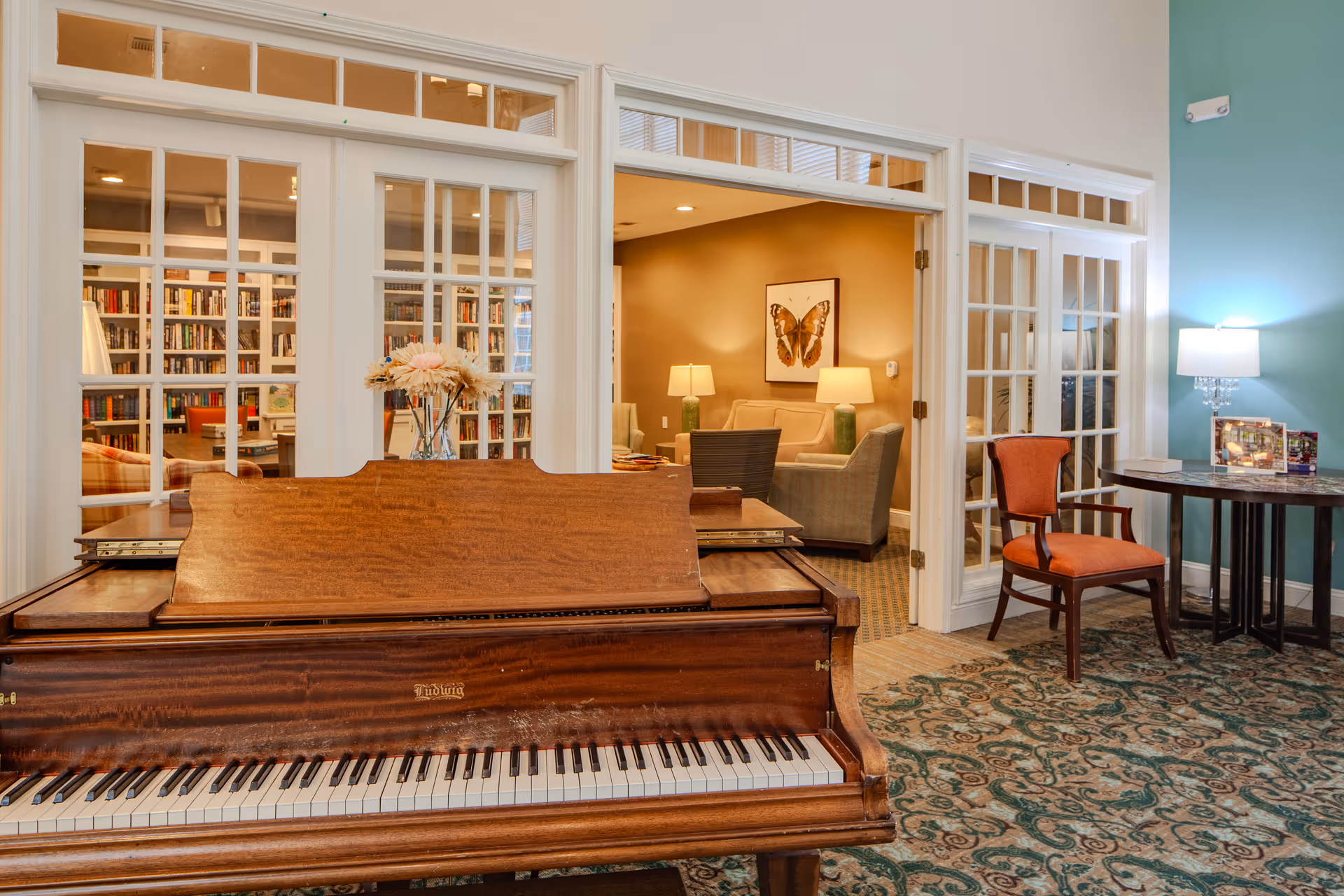 A wooden piano sits in a bright lobby with glass doors and seating beyond.