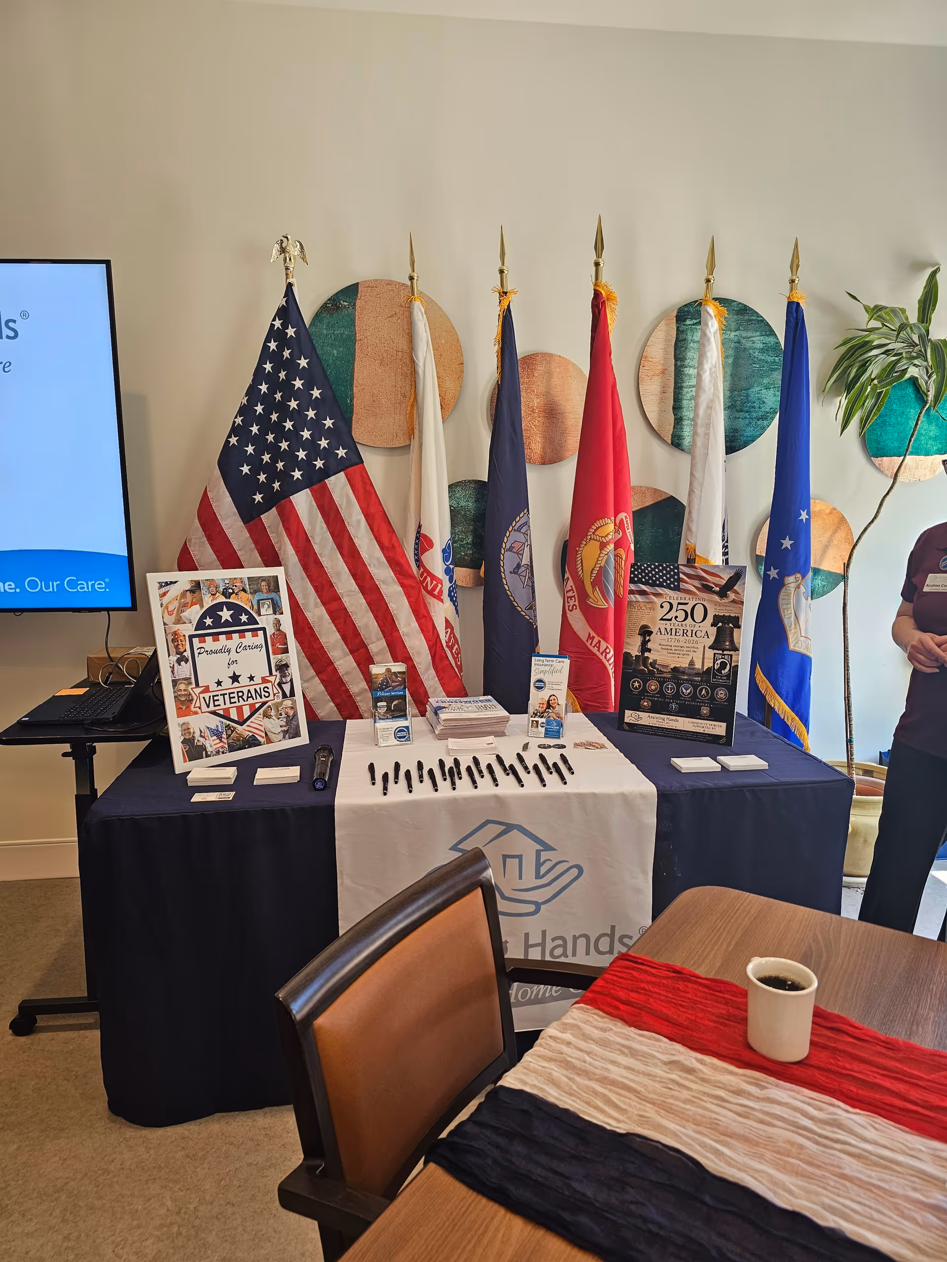 A row of flags behind a table with brochures and pens in a bright indoor setting.