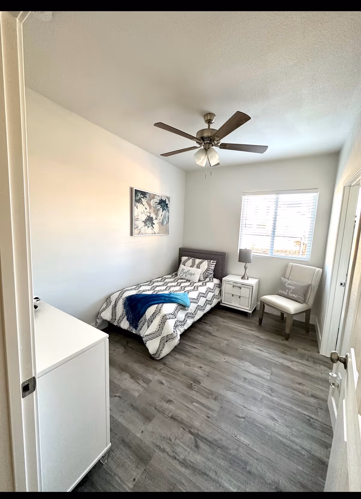 Cozy single bedroom with bed, nightstand, dresser, chair, and ceiling fan.