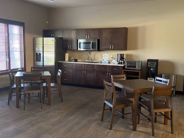 Communal kitchenette with dark wood cabinets, stainless appliances, and several wooden dining tables.