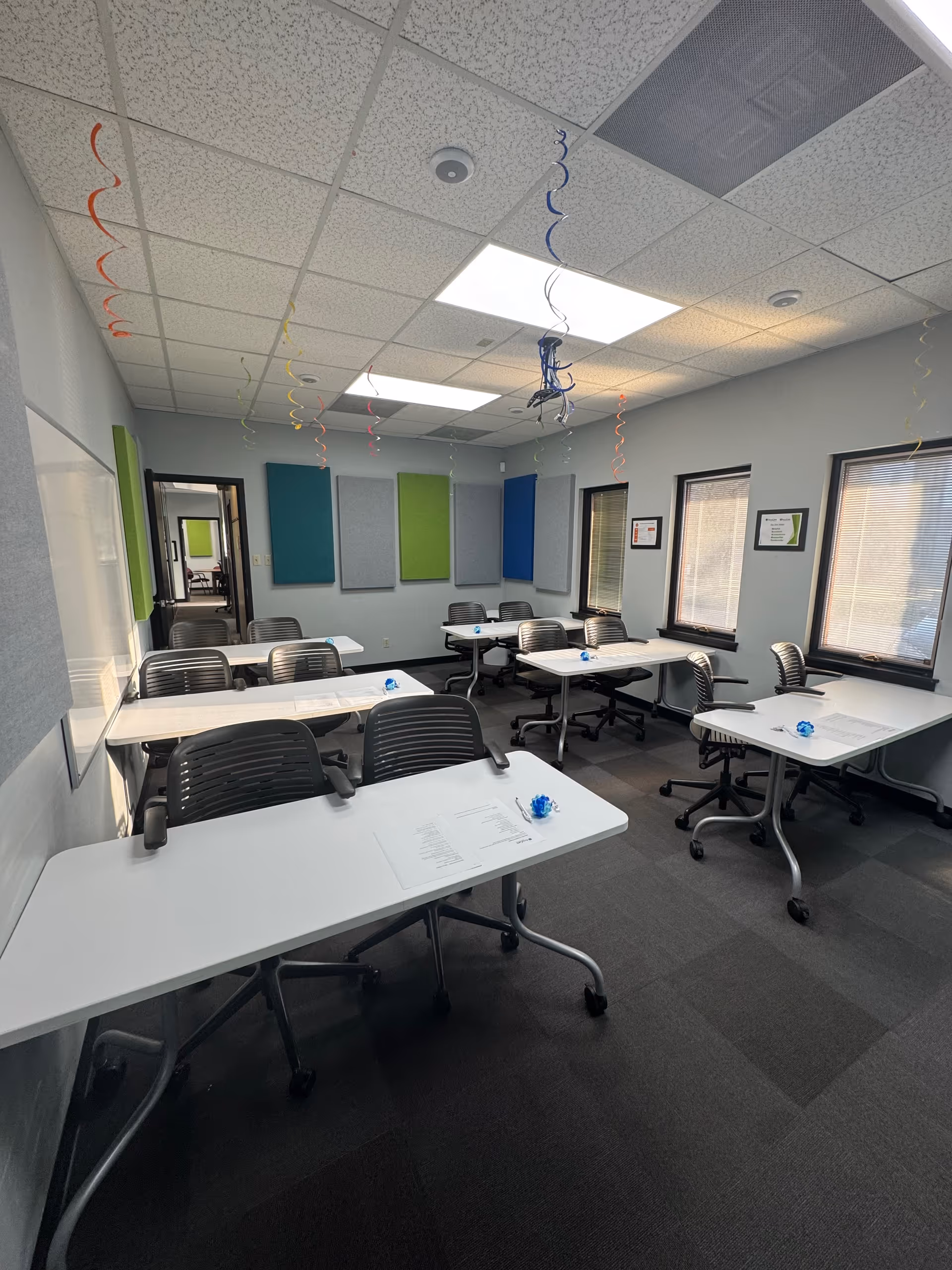 A classroom-style training room in AccuCare with white tables, rolling chairs, and colorful wall panels.