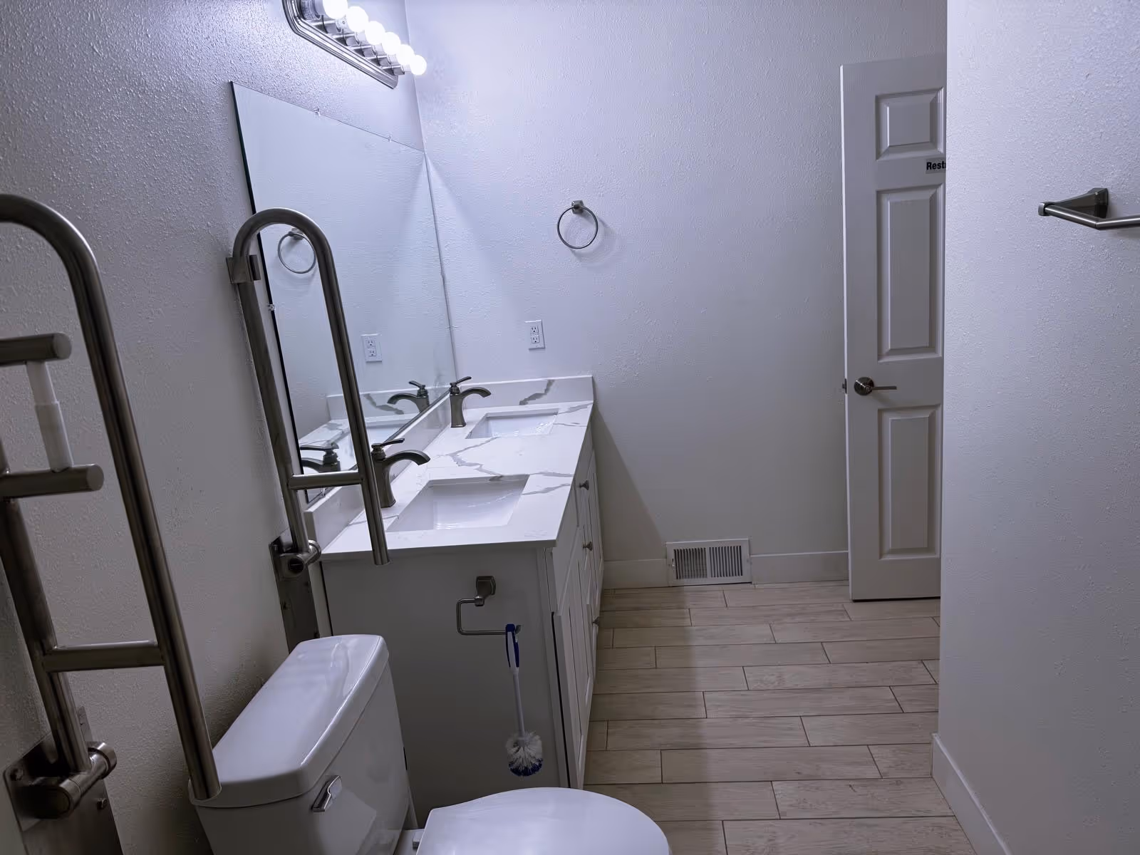 A modern shared bathroom with double sinks, a toilet, and safety grab bars.