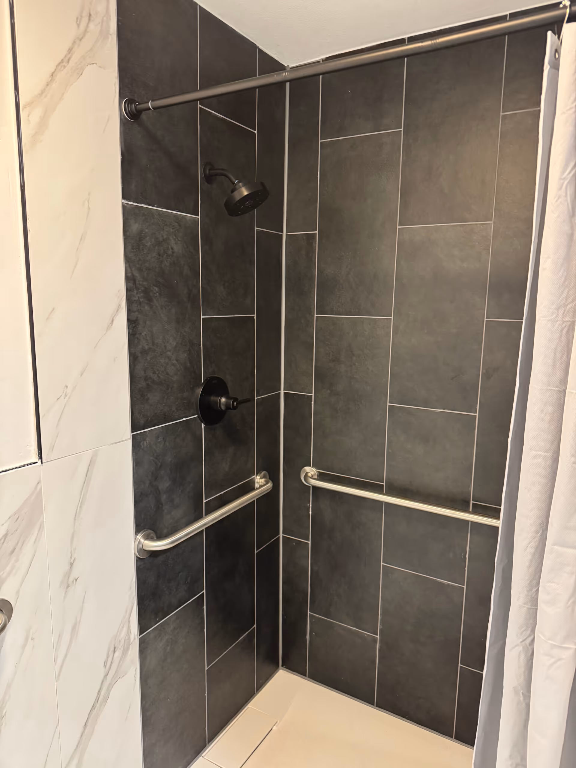 ADA-accessible bathroom shower with dark tiled walls, two grab bars, and a curtain.