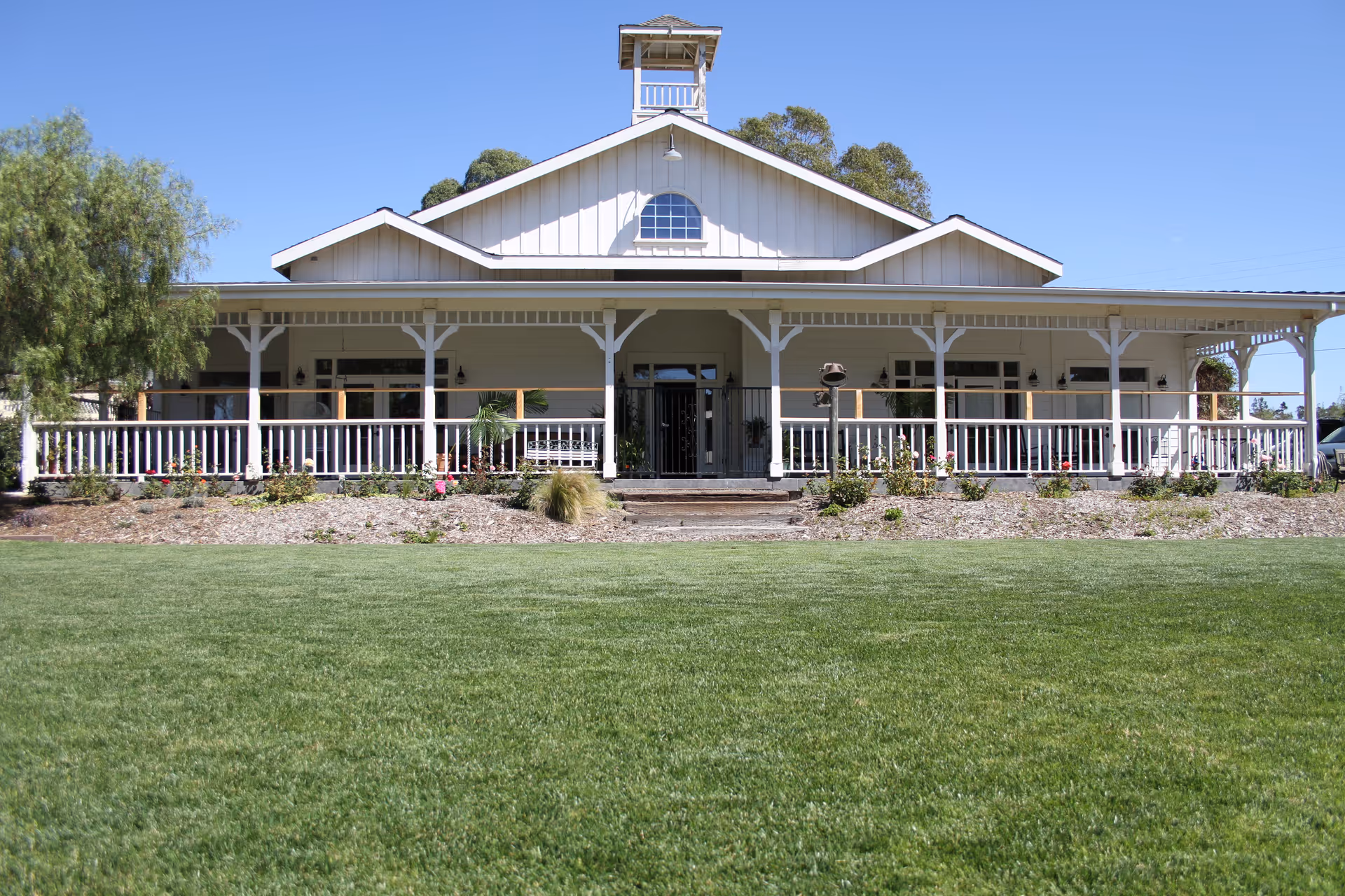 Exterior view of a light-colored senior living facility with a wraparound porch and lawn.