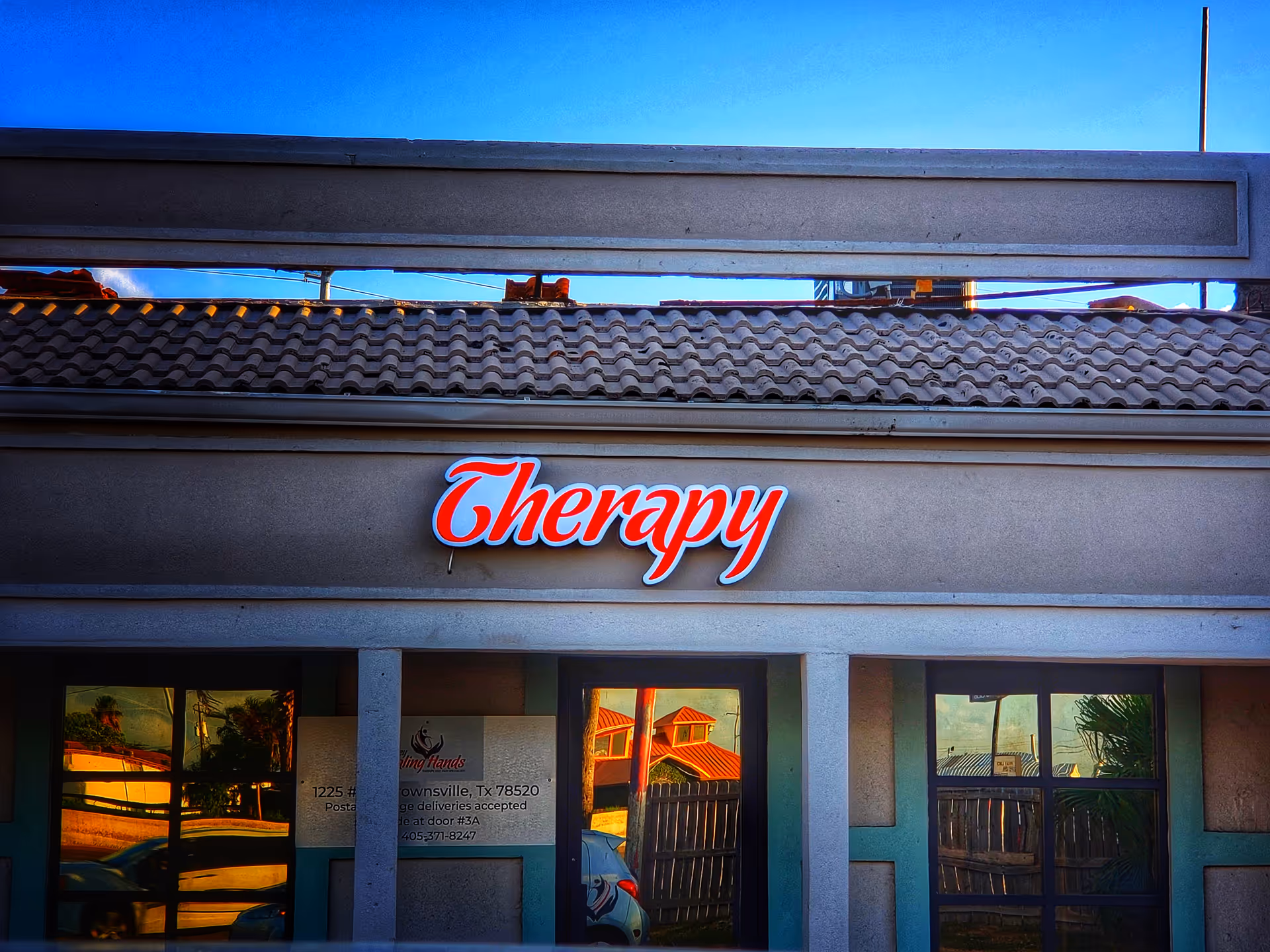 Front of a building with a red Therapy sign and glass doors beneath blue sky