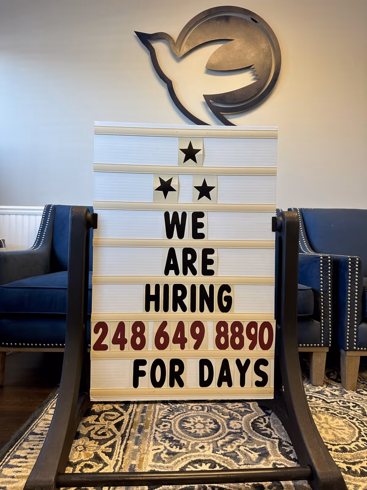 Lobby area with signboard 'We Are Hiring' beside blue upholstered chairs.