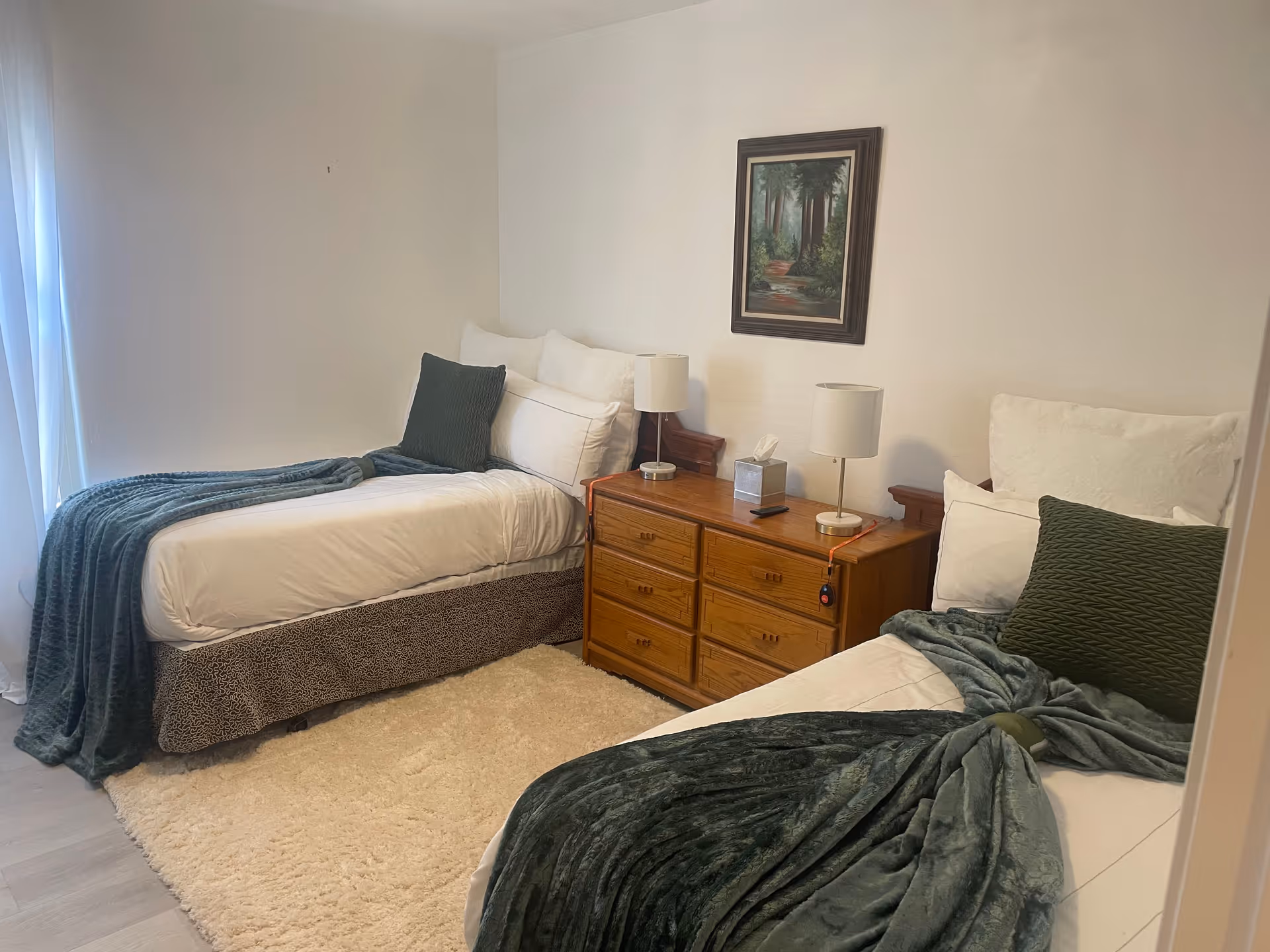 Two twin beds with white linens and green blankets flank a wooden dresser in a bedroom.