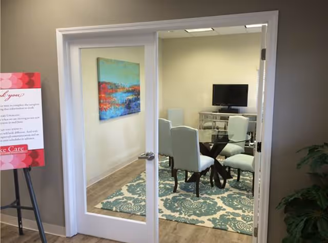 Glass-door meeting room with teal chairs around a glass table and a TV.