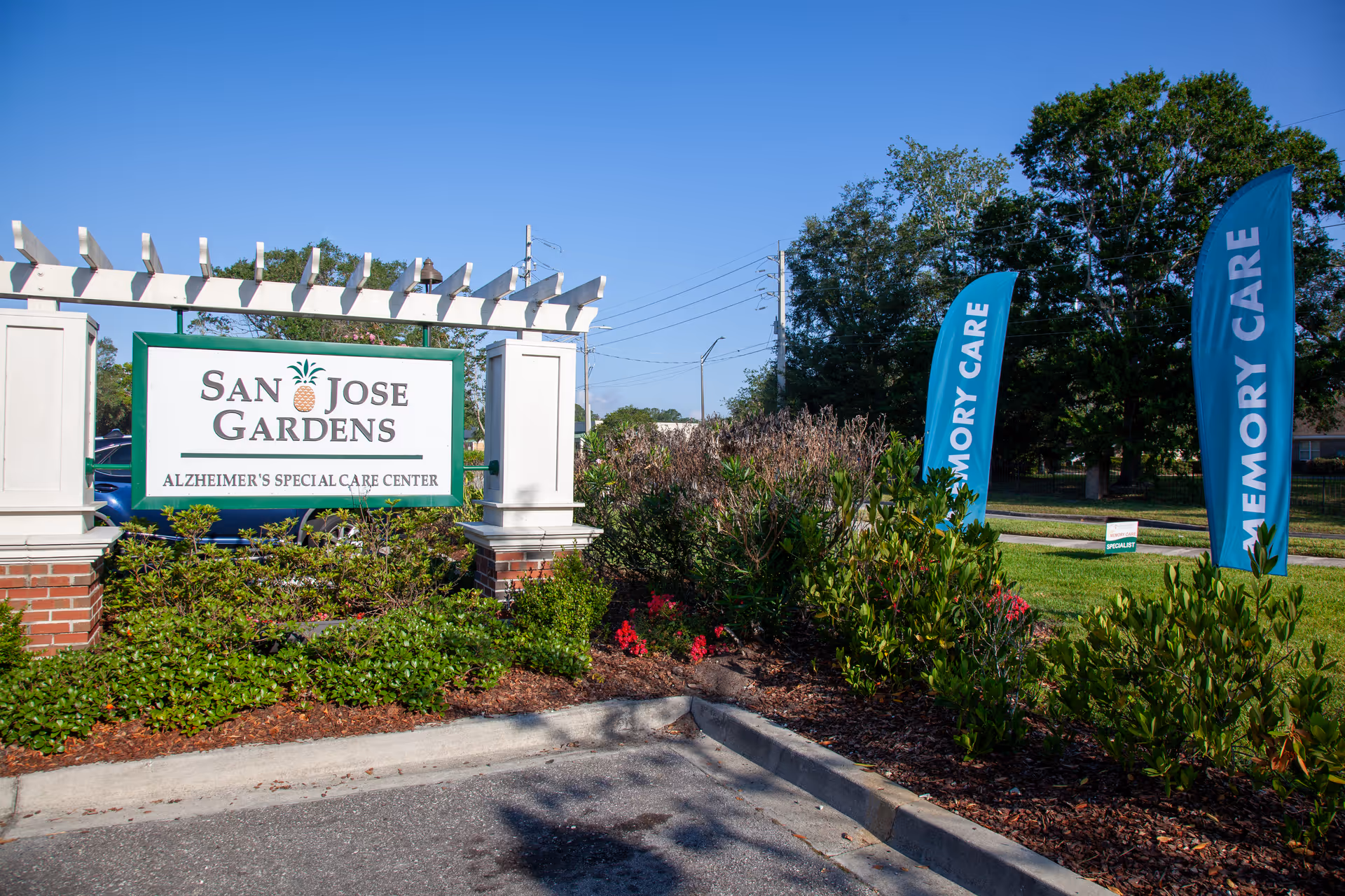 Exterior view of San Jose Gardens sign with blue flags and landscaping