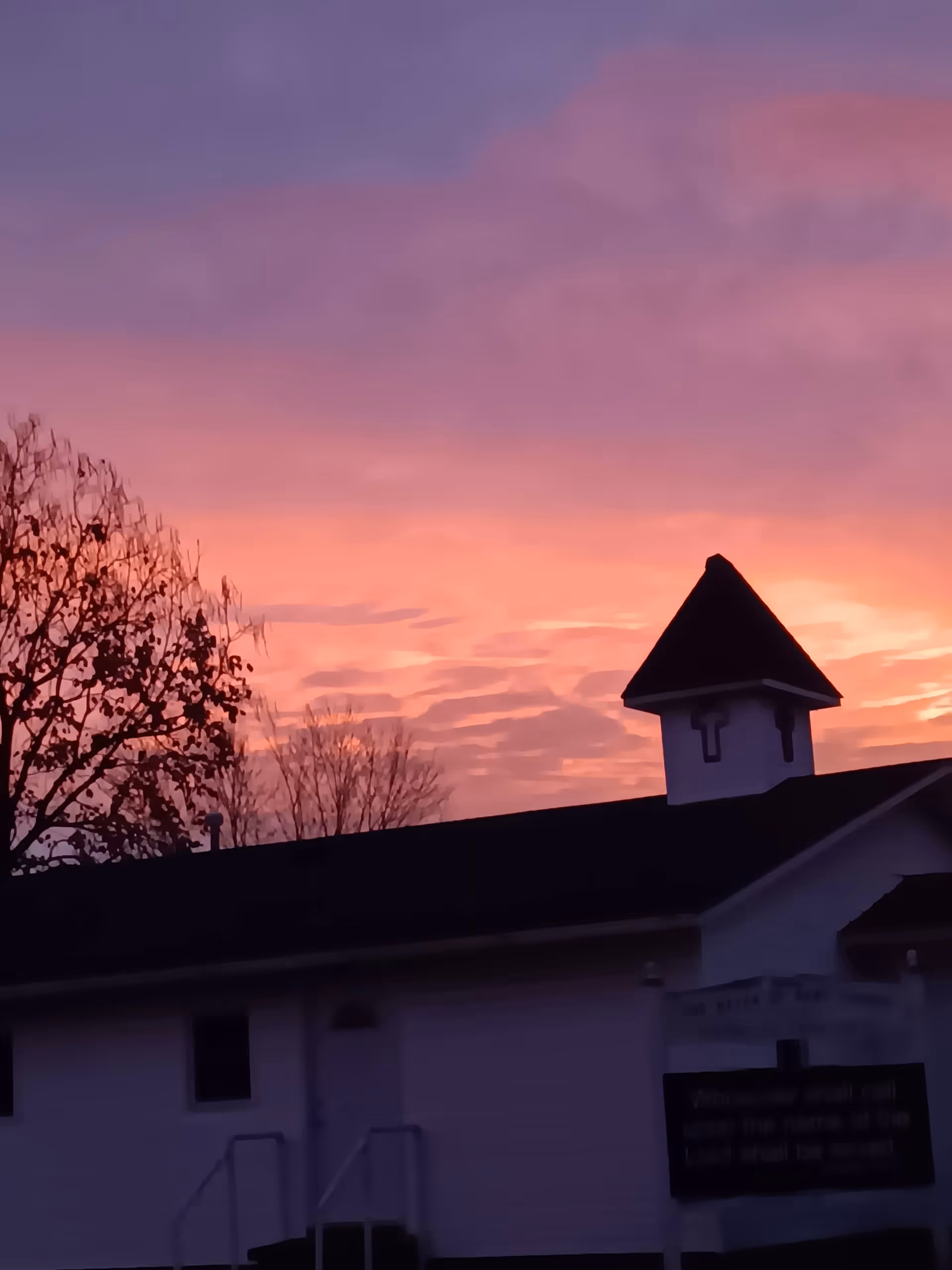 A building exterior with a tower-like roof against a pink sunset sky.