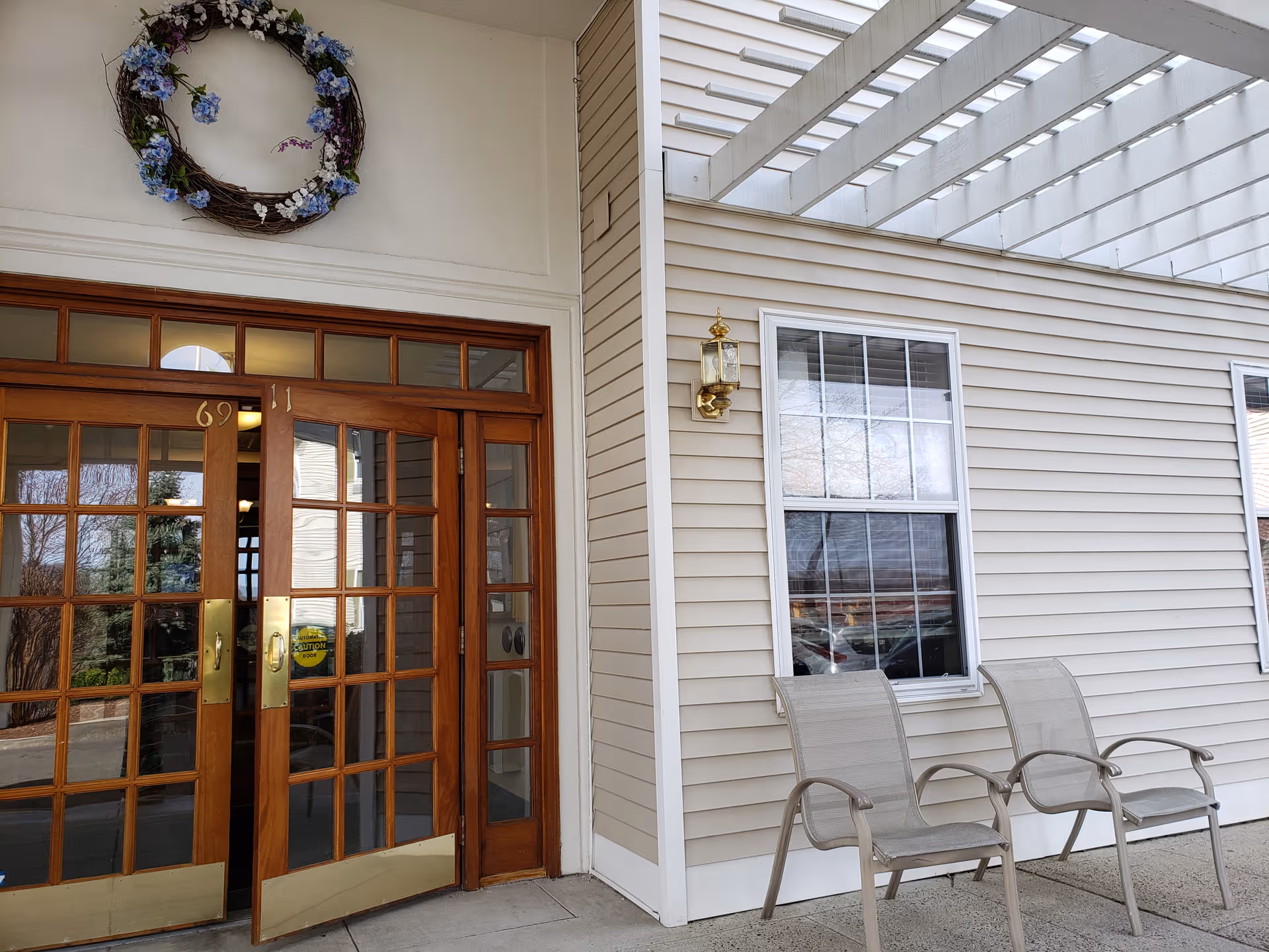 Front entrance of Spring Village Stratford with wooden doors, wreath, and two outdoor chairs.