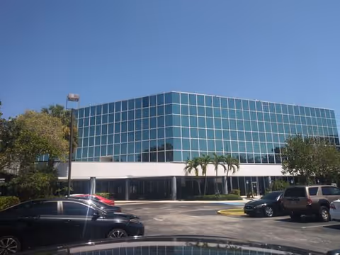 Modern glass-front CareMax Home Care building with parked cars and palm trees.