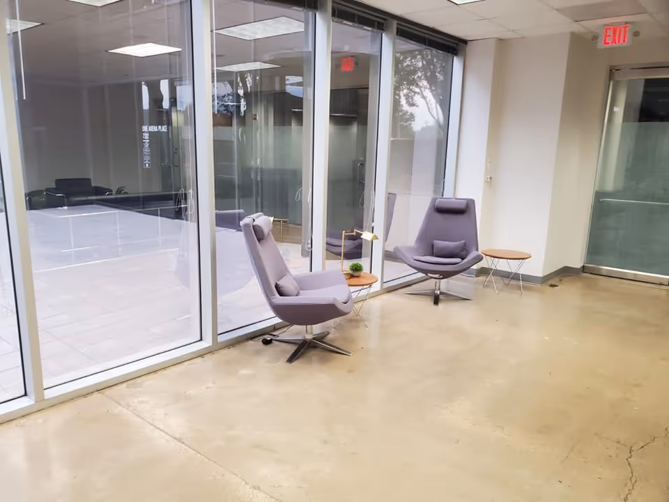 Modern indoor lounge with glass walls, purple chairs, and small tables in a senior care facility.