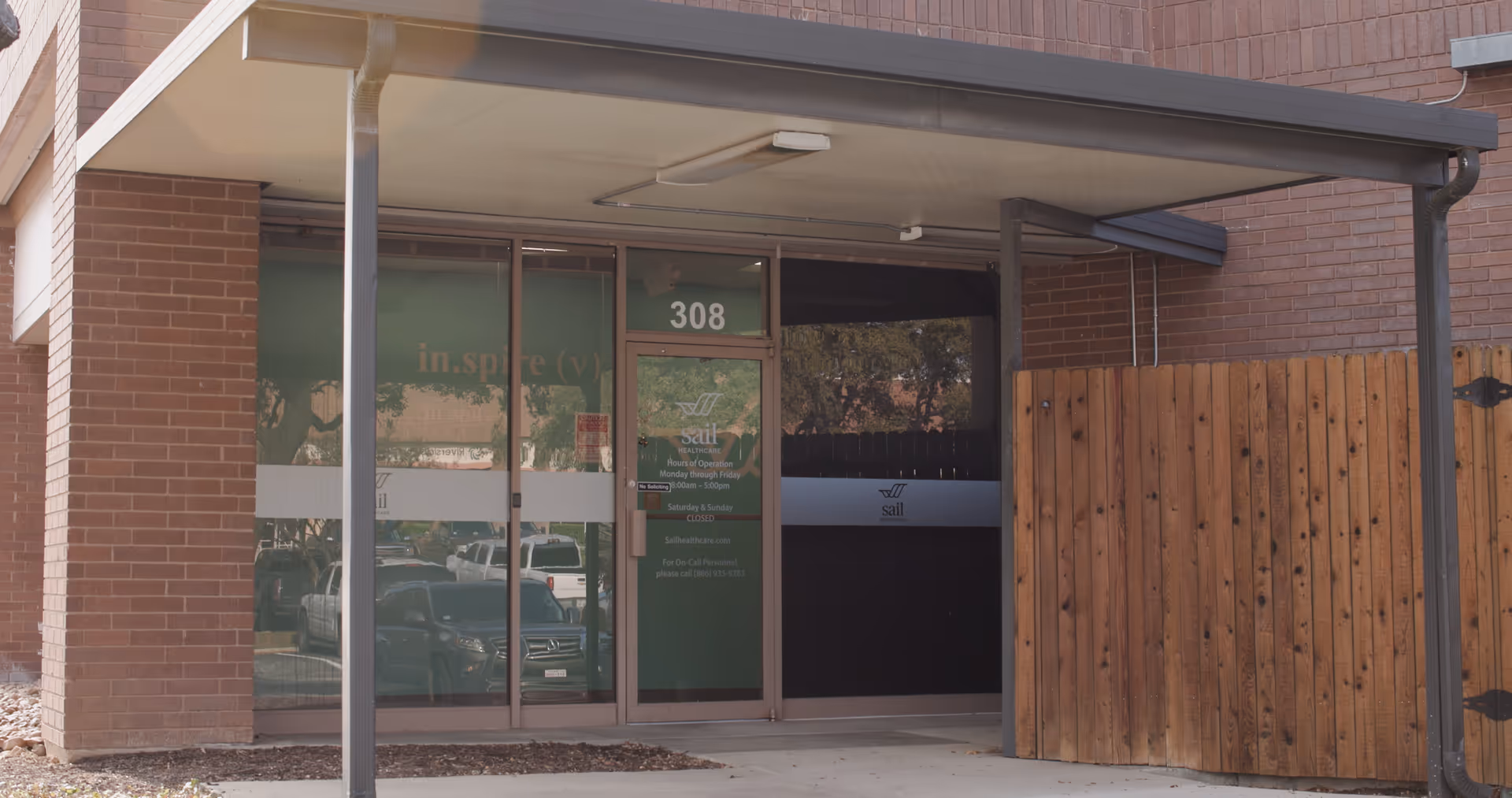 Exterior view of Sail Healthcare entrance with glass doors, brick walls, and a wooden fence.