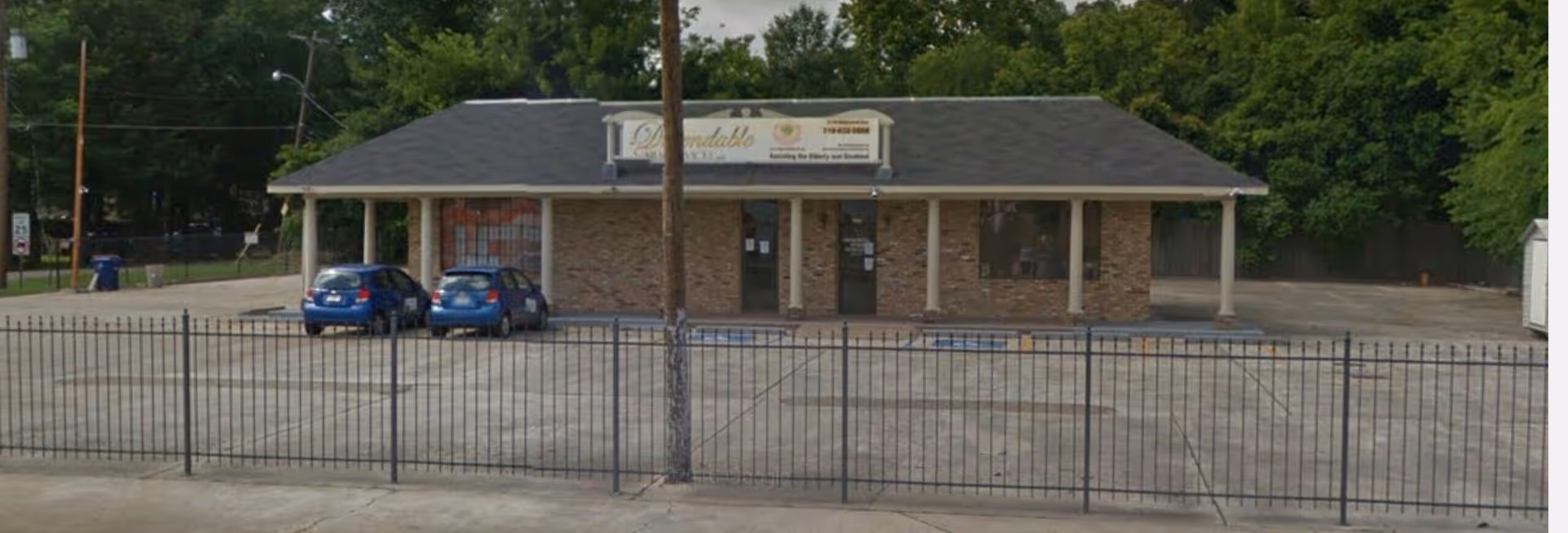 Single-story building exterior with a gated parking area and two blue cars.
