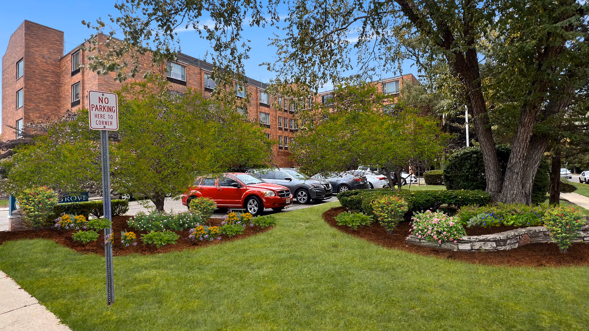 Brick senior living building with a landscaped front lawn, parking, and trees.