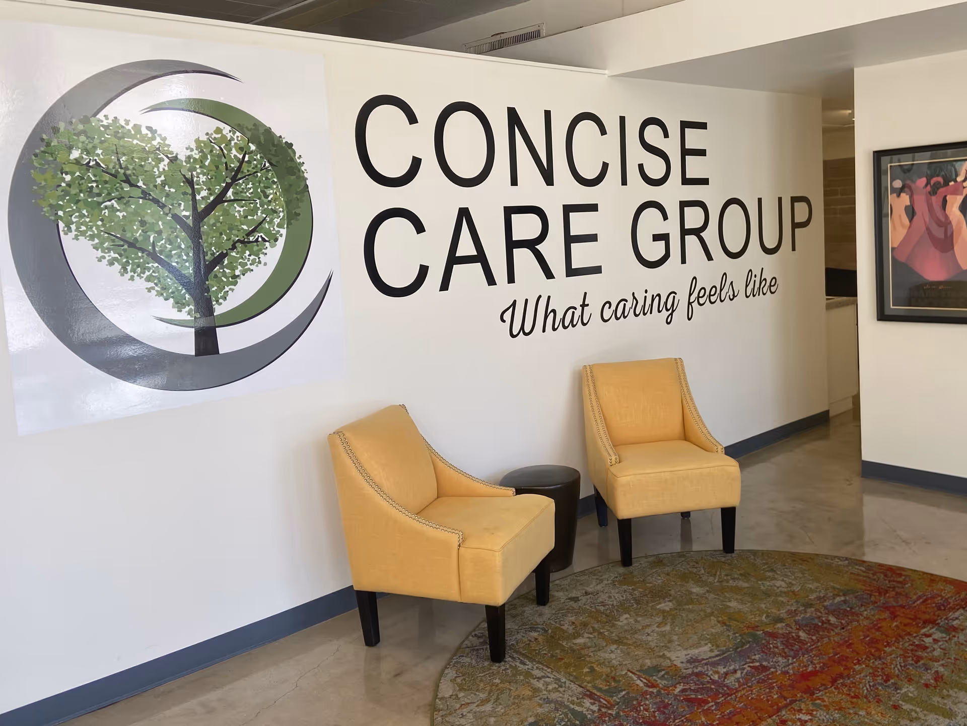 Lobby seating area with two beige chairs beside a wall sign reading Concise Care Group.