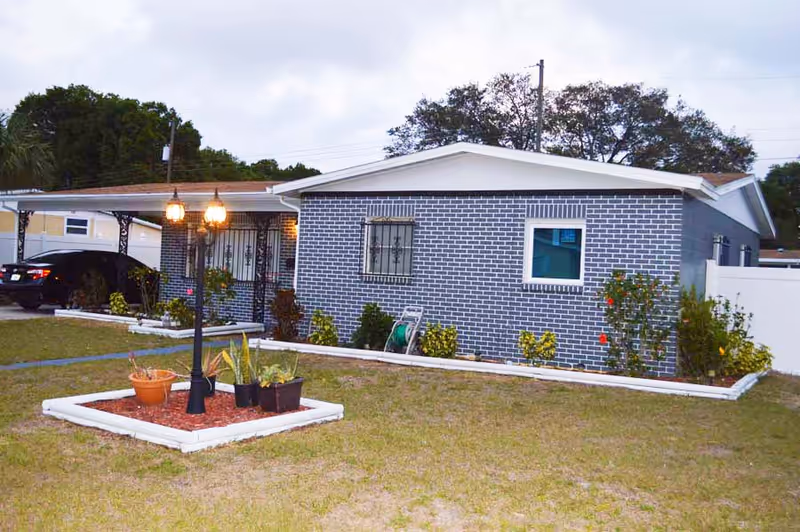 Single story blue brick building with a front yard, planters, and a lamp post.