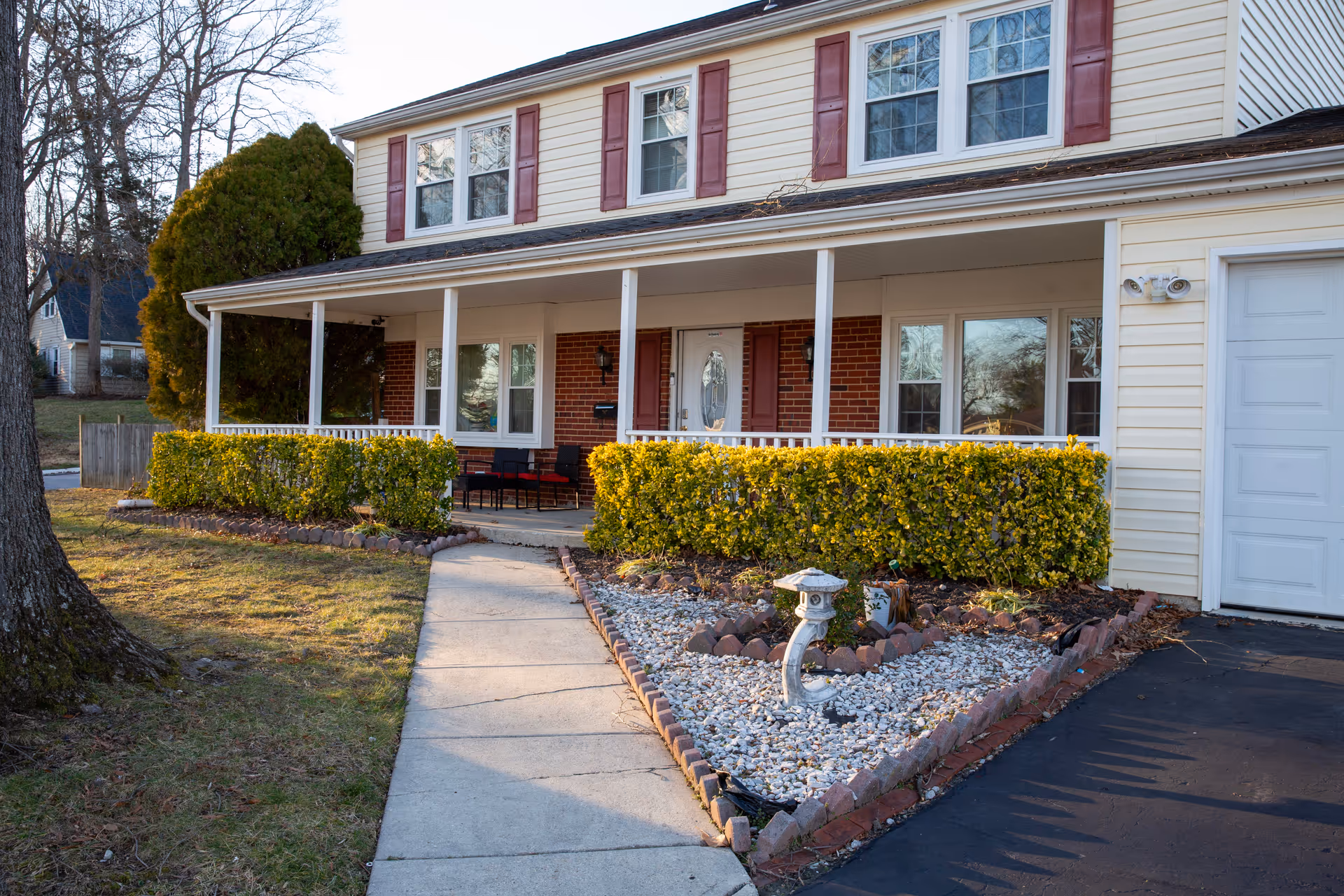 Two-story senior living facility with a wide front porch, trimmed hedges, and a curved walkway.