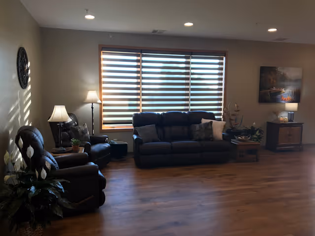 Cozy senior living facility living room with leather sofas, lamps, and blinds.