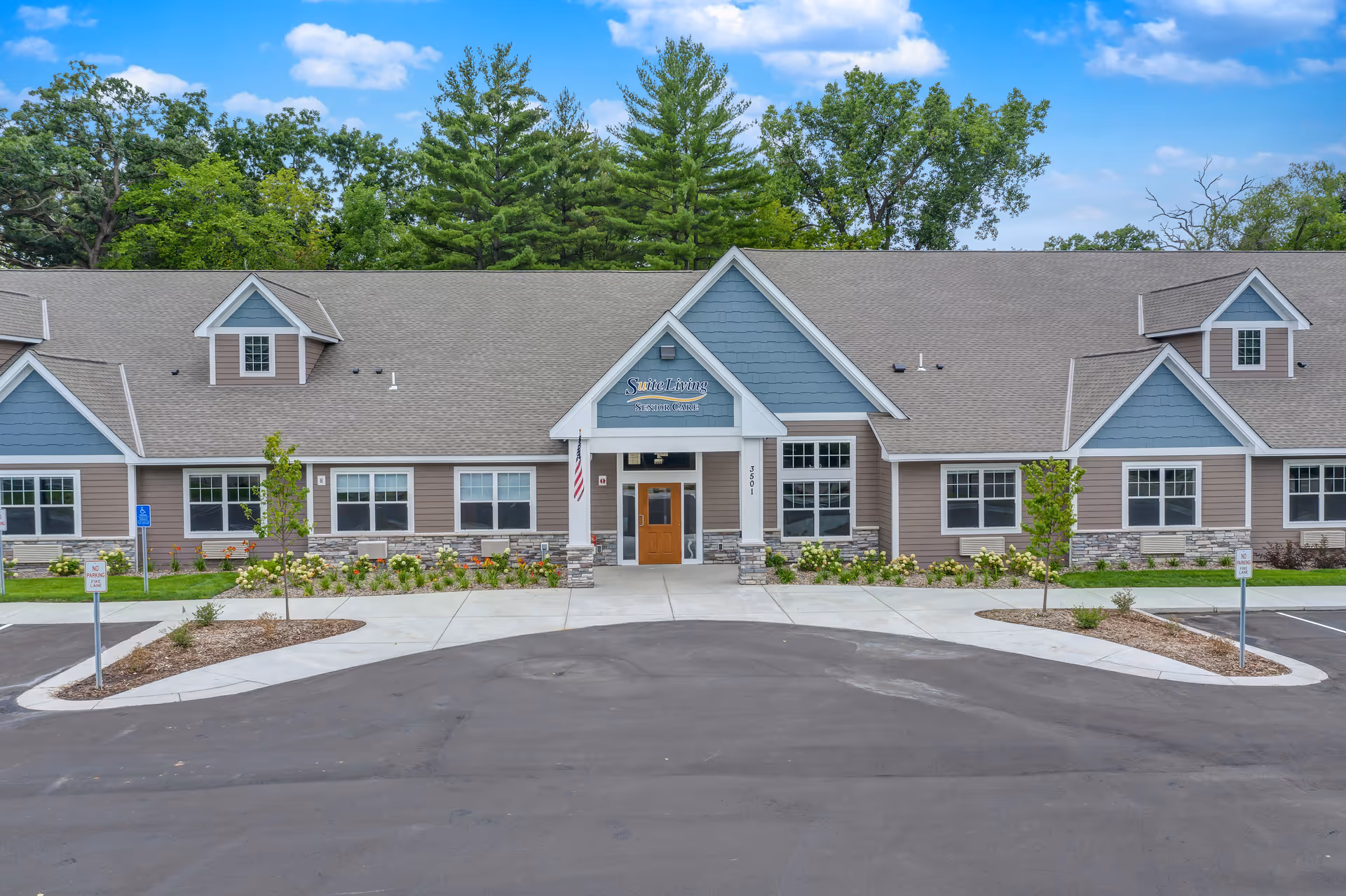 Front exterior of a single-story senior living facility with a central entrance, landscaped beds, and a paved driveway.