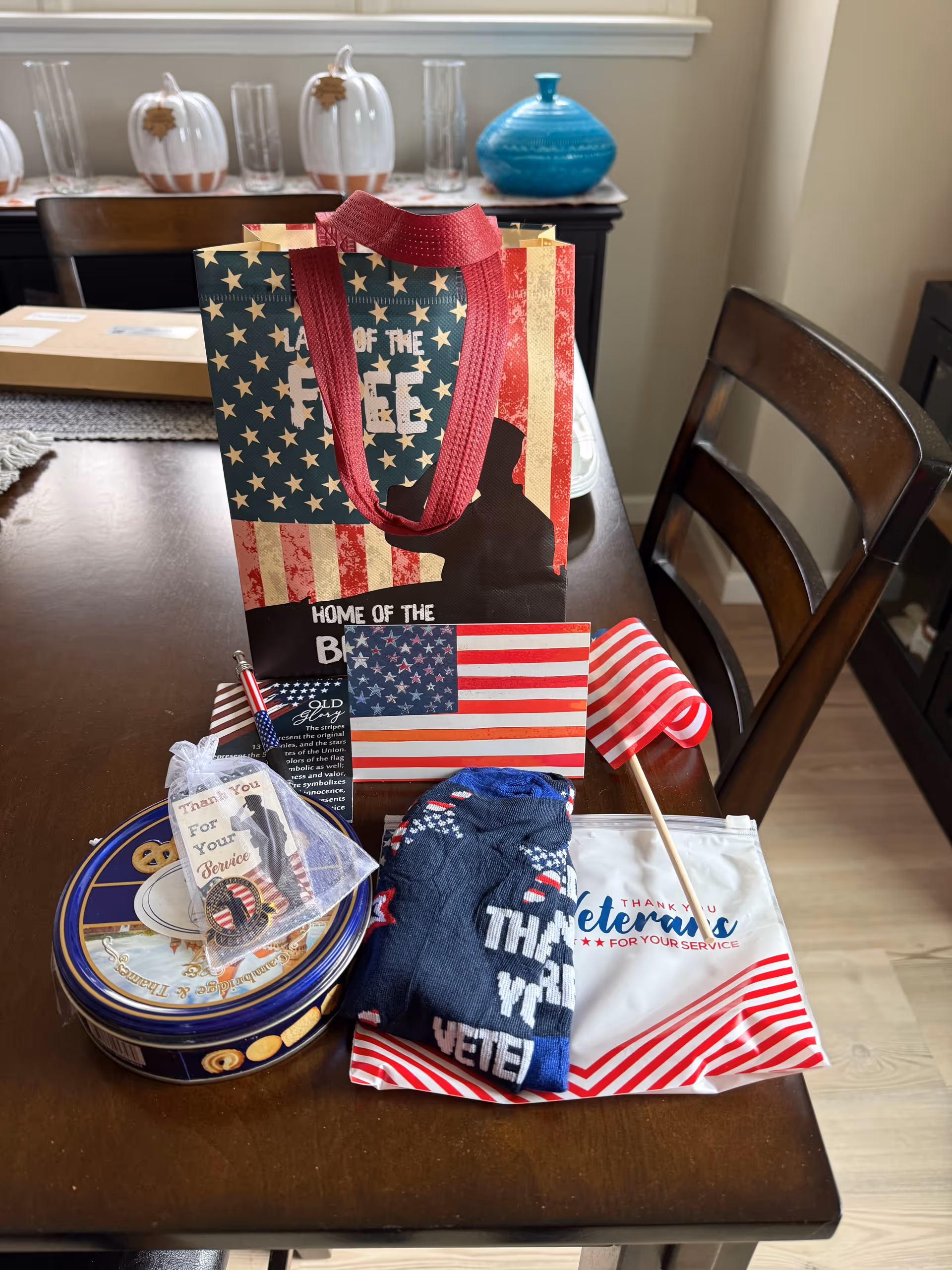 Patriotic gift bag and American flags on a wooden dining table indoors.