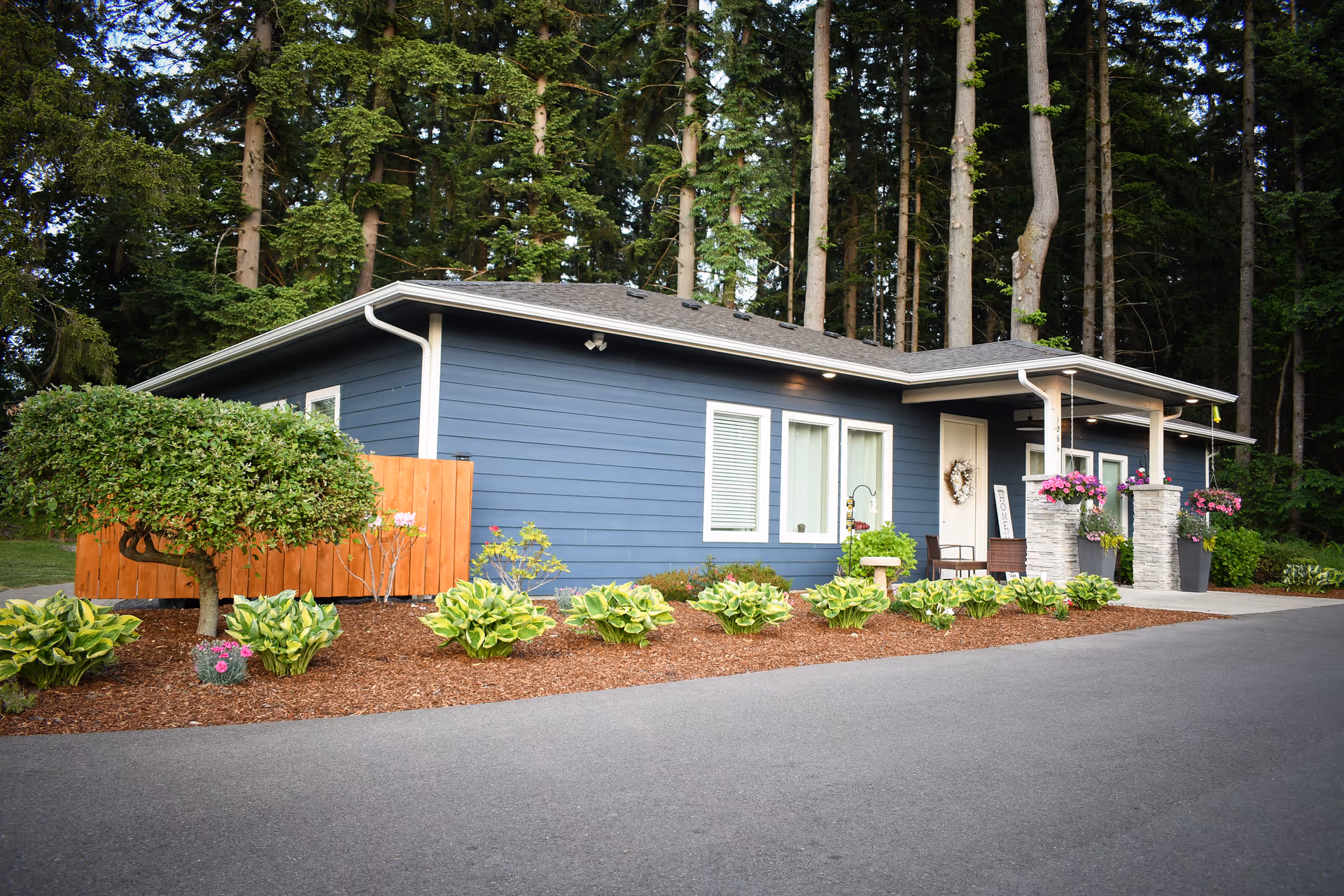 Blue single-story building with white trim, front porch, and landscaped garden beside a driveway.