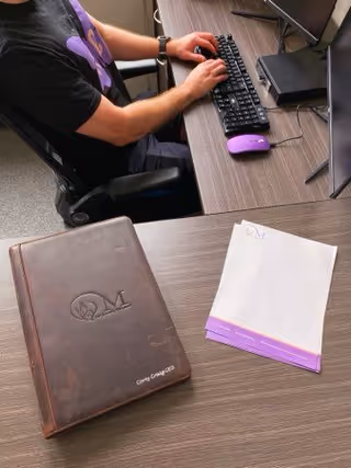 Person typing at a desk with a monitor, keyboard, and Monarch-branded notebook.
